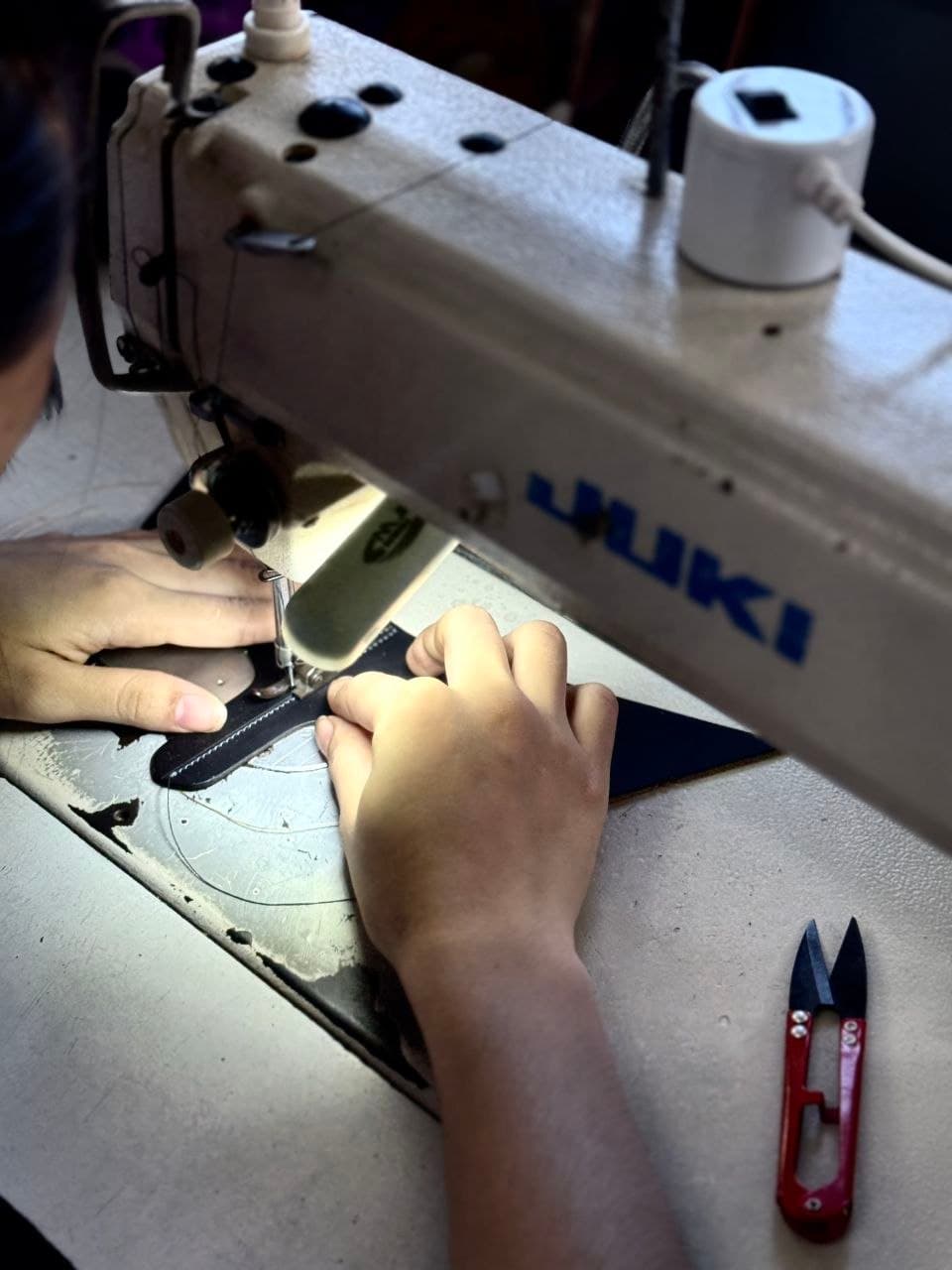 An artisan stitching leather straps at the sewing machine